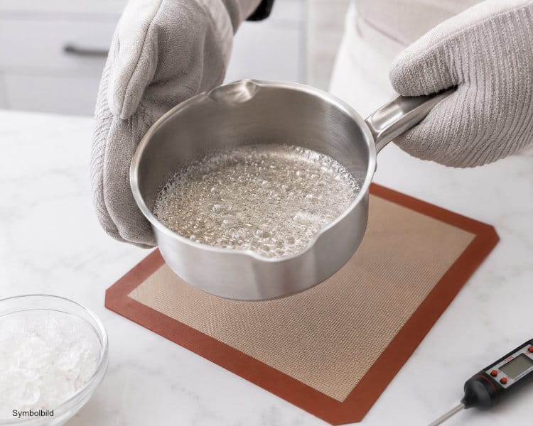 Hände mit Hitzeschutzhandschuhen lösen Isomalt in einem Topf bei kontrollierter Temperatur auf
